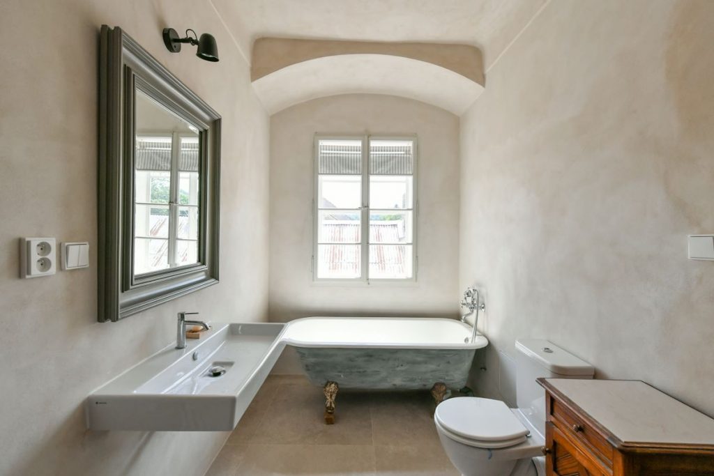 Kúpeľňa s voľne stojacou vaňou vo vintage štýle a veľkým oknom v rekonštruovanej fare v Chudeniciach.