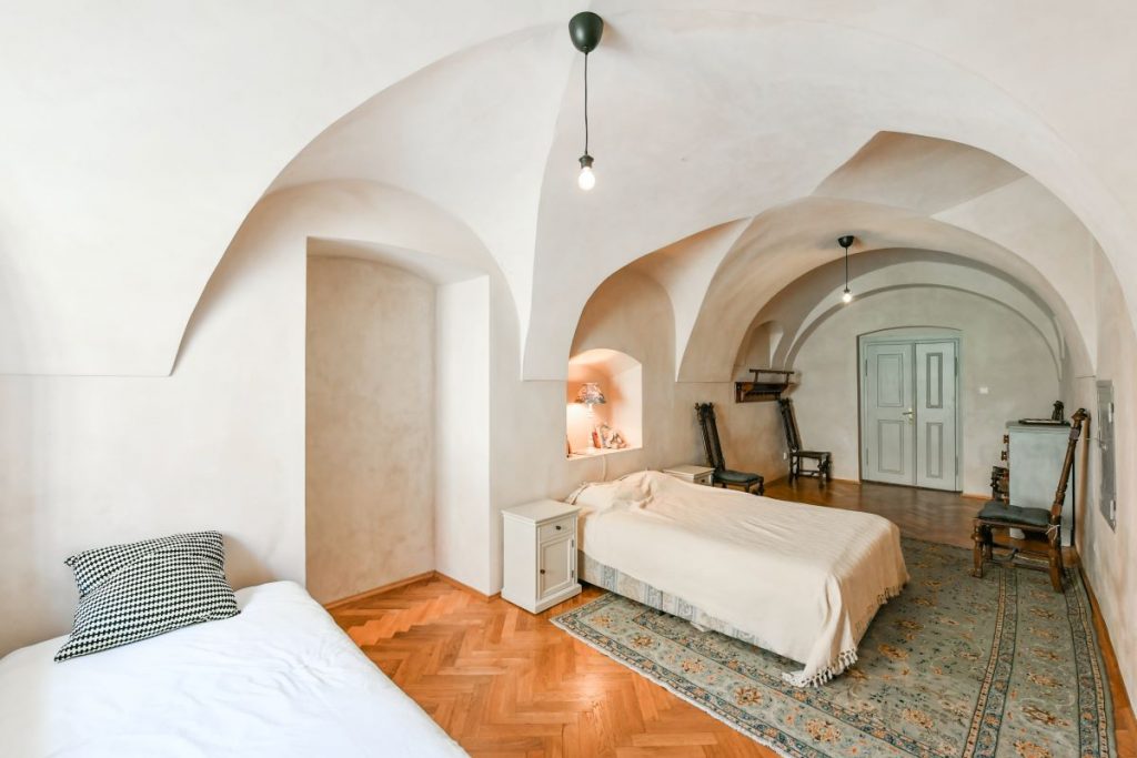 Spálňa s klenutým stropom, dvoma posteľami a historickým zariadením v zrekonštruovanej fare v Chudeniciach.