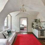 Obývacia izba s tradičným kachľovým sporákom a bielym gaučom v zrekonštruovanej fare v Chudeniciach.
