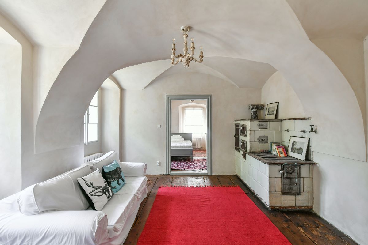 Obývacia izba s tradičným kachľovým sporákom a bielym gaučom v zrekonštruovanej fare v Chudeniciach.
