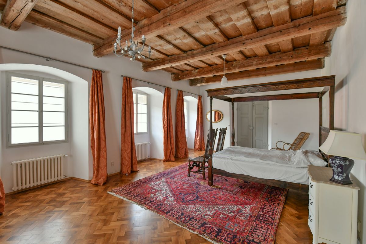 Priestranná spálňa s drevenou posteľou s baldachýnom, vzorovaným kobercom a historickým nábytkom v zrekonštruovanej fare v Chudeniciach.