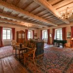 Priestranná sála s drevenými trámami a historickým nábytkom v zrekonštruovanej fare v Chudeniciach.