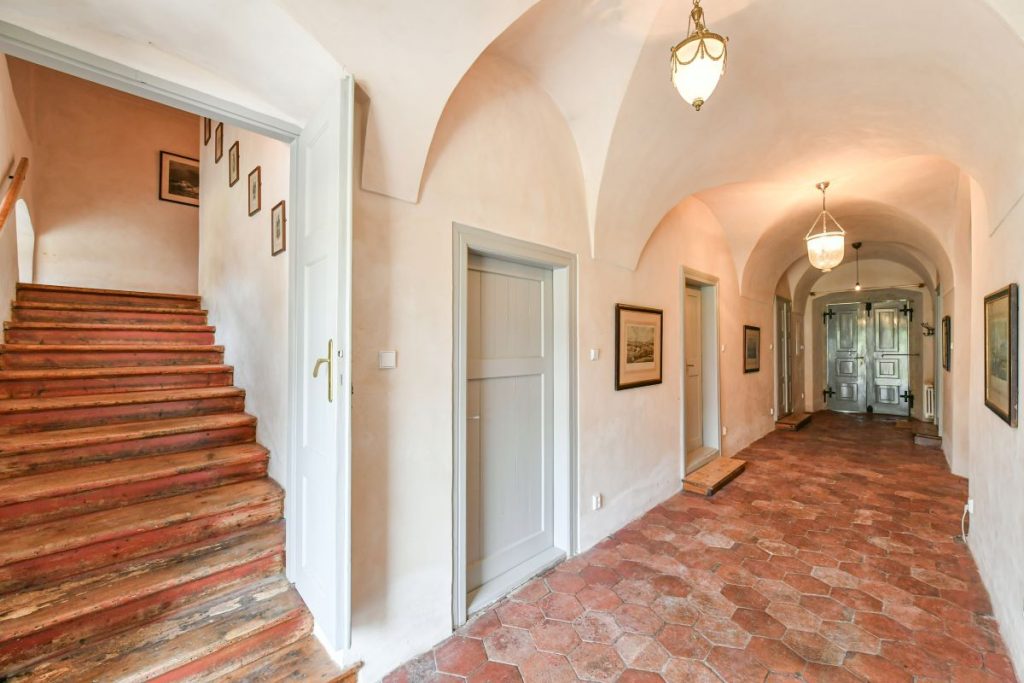 Chodba s klenutým stropom, viacerými dverami a drevenými schodmi na poschodie v rekonštruovanej fare v Chudeniciach.