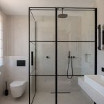 Moderne zariadená kúpeľňa so sprchovacím kútom s čiernym rámom a toaletou.