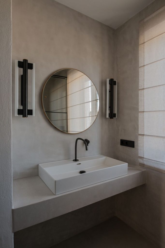 Moderne zariadená kúpeľňa s umývadnom na murovanej polici a okrúhlym zrkadlom.