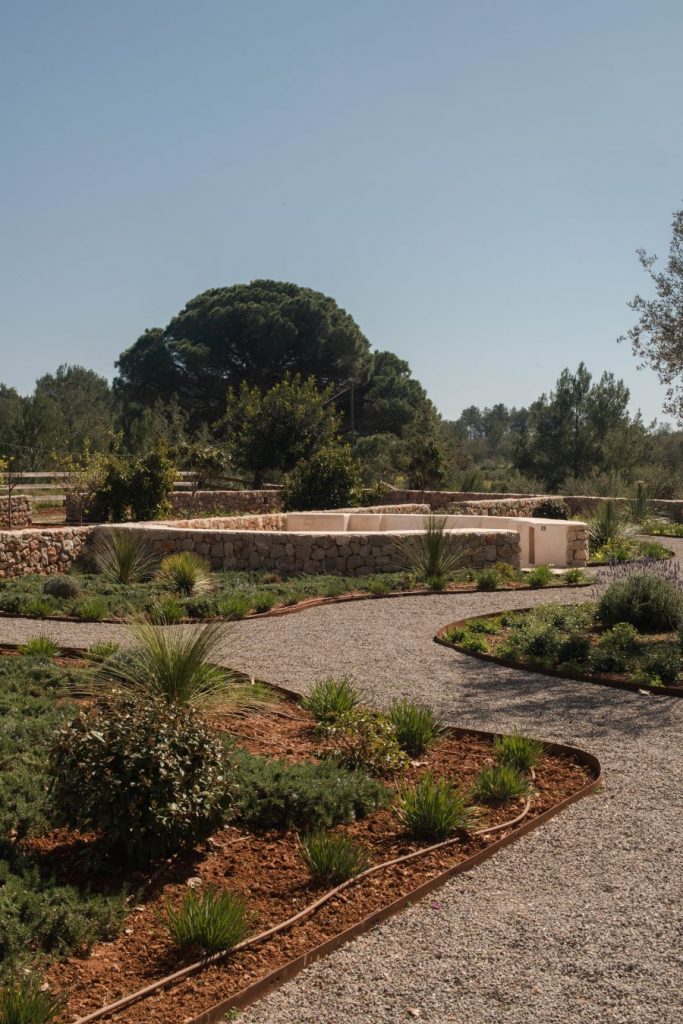 Kľukatý štrkový chodník na rozľahlej záhrade s upravenými záhonmi pri dome na Ibize.
