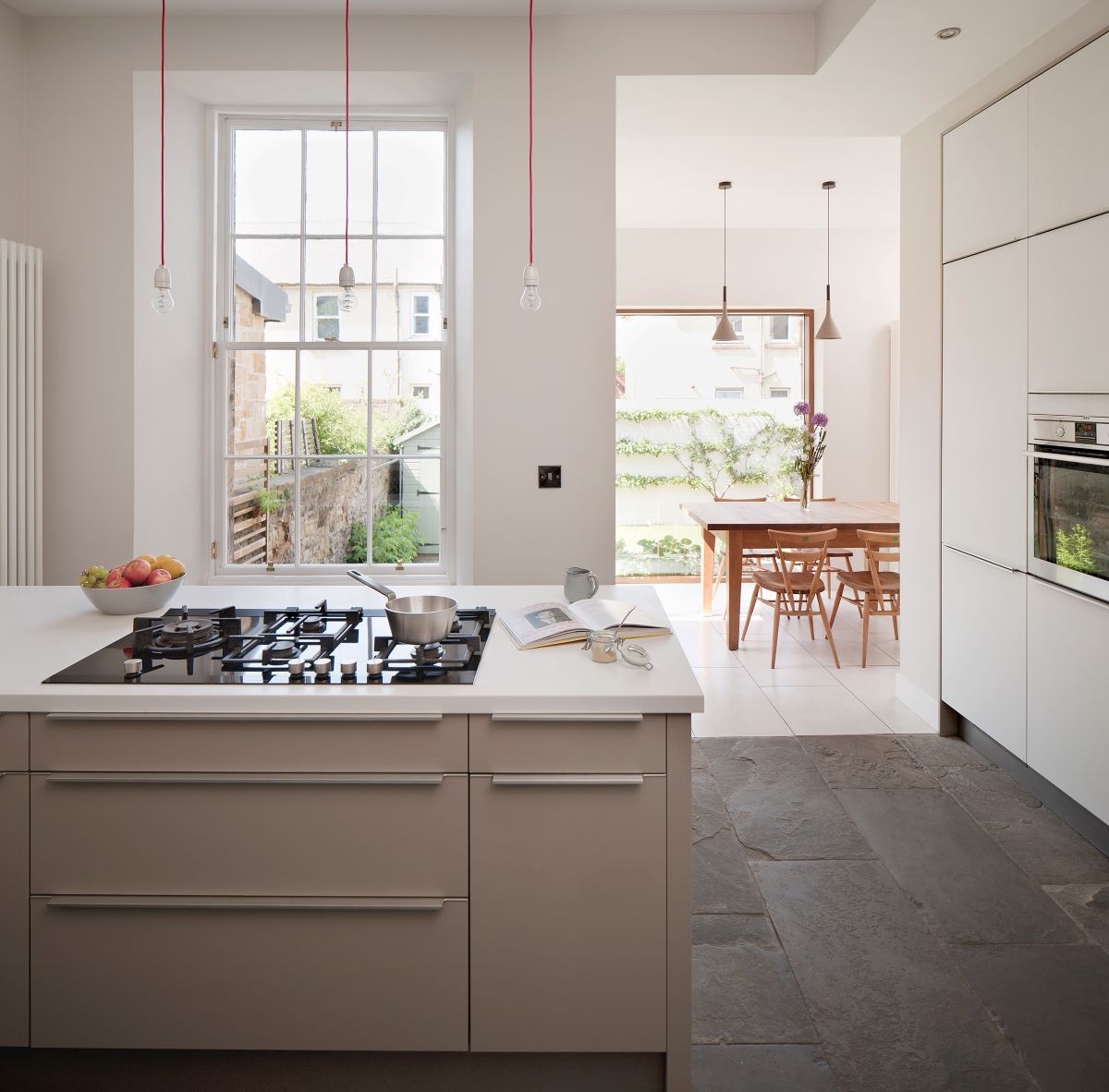 Moderná kuchyňa s bielymi skrinkami, veľkým oknom a jedálenským kútom.