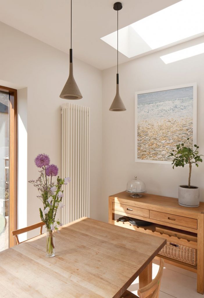 Svetlá jedáleň s dreveným nábytkom, modernými lampami a obrazom na stene.