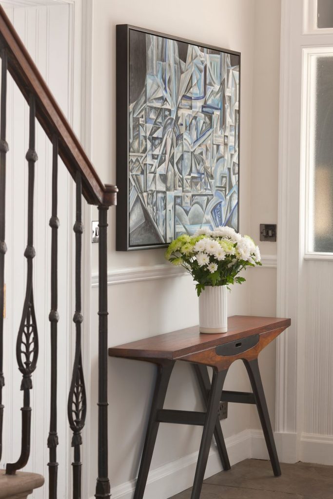 Vstupná chodba so stolom a obrazom, zdobená kvetmi v zrekonštruovanom historickom dome.