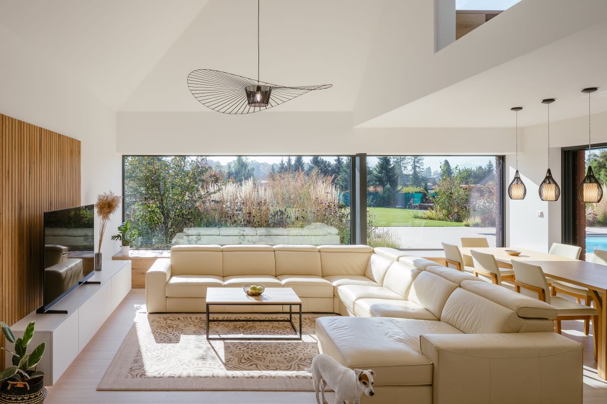 Moderne zariadená obývačka s veľkou svetlou sedačkou, jedálenským stolom so svetlými stoličkami a veľkorozmerným oknom so vstupom na terasu.
