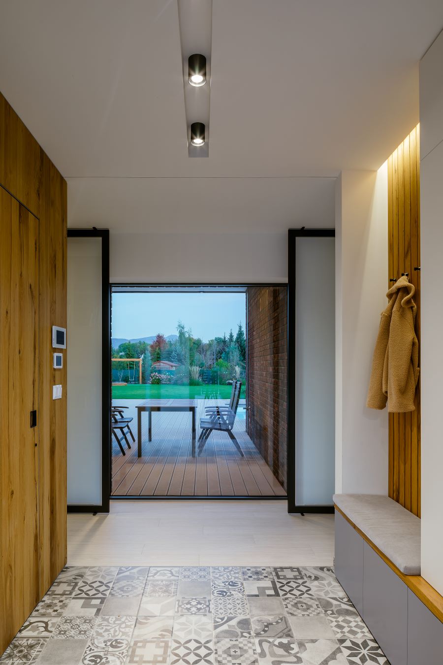 Nadčasovo zariadená vstupná časť domy s drevom obloženou i vešiakovou stenou a veľkorozmerným oknom s výhľadom na terasu.