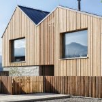 Moderný drevený dom v minimalistickom dizajne s veľkými oknami a výhľadom na hory.