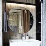 Minimalistická kúpeľňa s dreveným obložením, veľkým okrúhlym zrkadlom a moderným umývadlom.