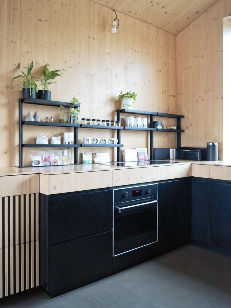Štýlová kuchyňa s dreveným obložením a čiernymi skrinkami a otvorenými policami s rastlinami a kuchynským príslušenstvom.