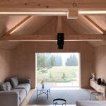 Obývacia izba s vysokým dreveným stropom, veľkým oknom, nadčasovými sedačkami a minimalistickým nábytkom.