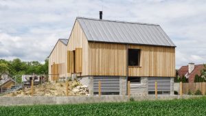 Moderný drevený dom s oceľovou strechou a veľkými oknami, zasadený v prírodnom prostredí.