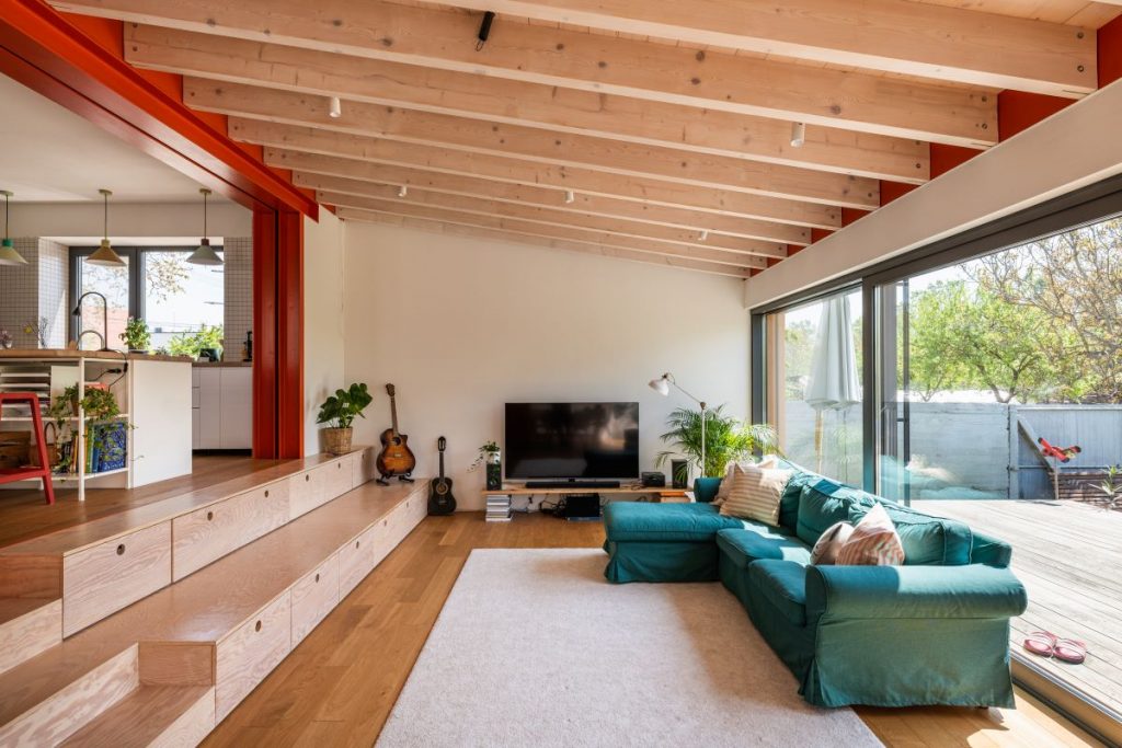 Moderná obývacia izba s televízorom a modrozelenou sedačkou pri veľkoformátovom vstupe na terasu.