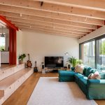 Moderná obývacia izba s televízorom a modrozelenou sedačkou pri veľkoformátovom vstupe na terasu.