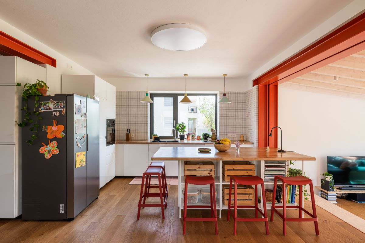 Moderná kuchyňa s bielou linkou a kuchynským ostrovom s drevenou pracovnou doskou a červeným barovými stoličkami.