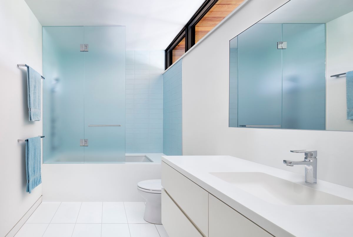 Elegantná kúpeľňa v minimalistickom dizajne s preskleným sprchovacím kútom a veľkým zrkadlom.