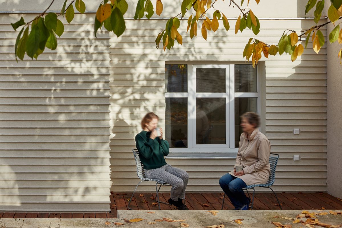 Dvaja ľudia, ktorí sedia an stoličkách na terase a rozprávajú sa.