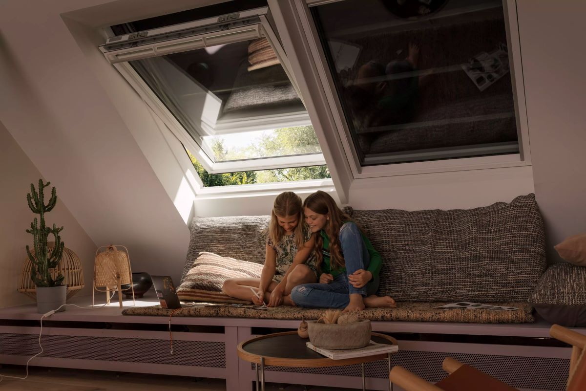 Dve dievčatá sedia na sedačke v podkrovnej izbe pod oknami so žauziami.