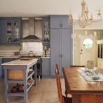 Vidiecky zariadená kuchyňa s drevenou kuchynskou linkou v sivomodrej farbe a drevený jedálenský stôl s vintage lustrom.