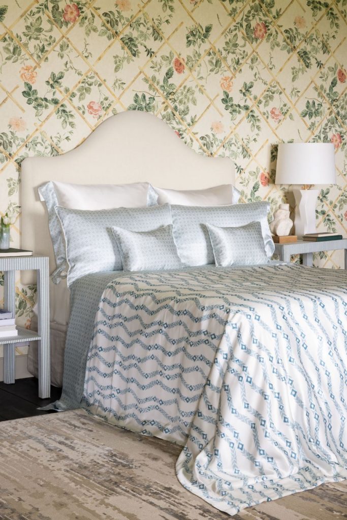 Spálňa zariadená vo vidieckom štýle s posteľou s vysokým čelom, vzorovanou posteľnou bielizňou a kvetovanými tapetami.