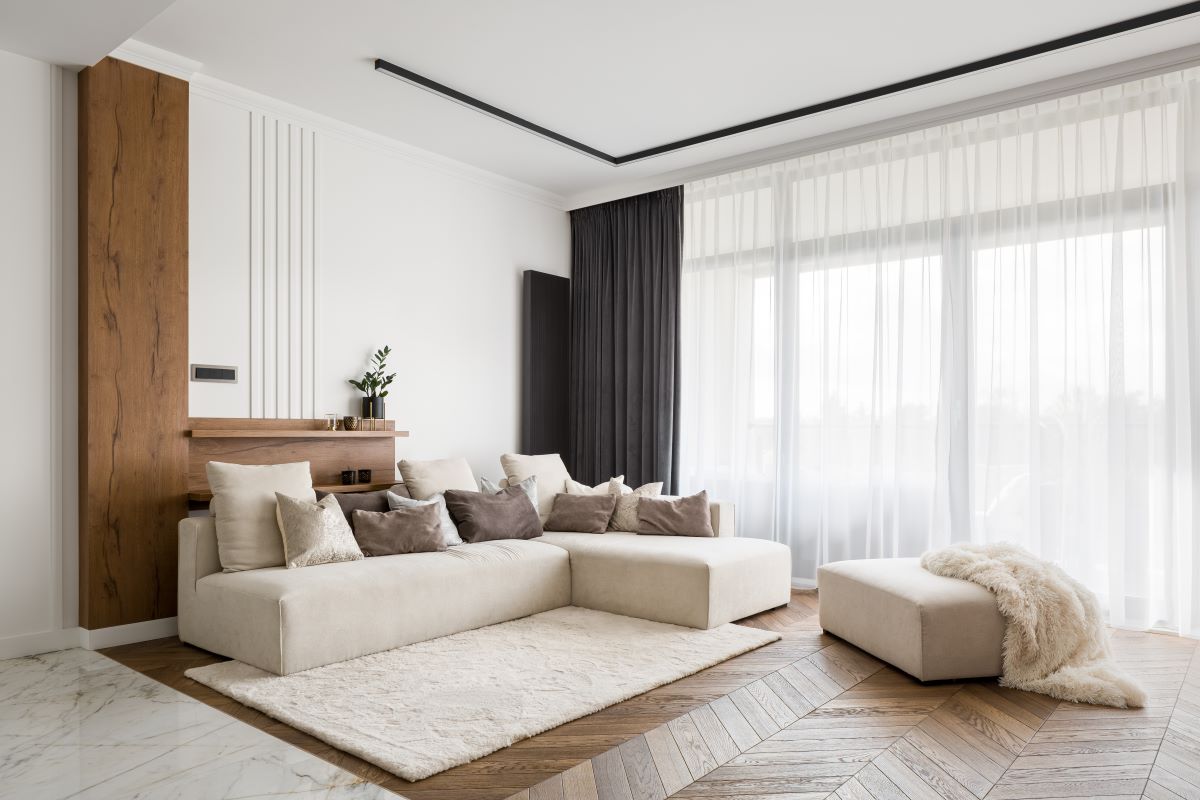 Nadčasová obývačka vo svetlých prírodných farbách a oknom so záclonou a tmavým závesom.