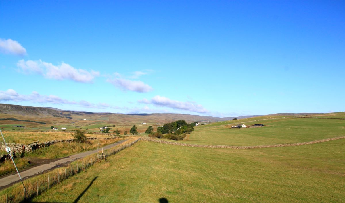 Panoramatický výhľad na vidiecku krajinu so zelenými lúkami a kopcami a modrou oblohou.