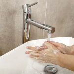 Detail na človeka, ktorý si umýva ruky pod tečúcou vodou v umývadle.