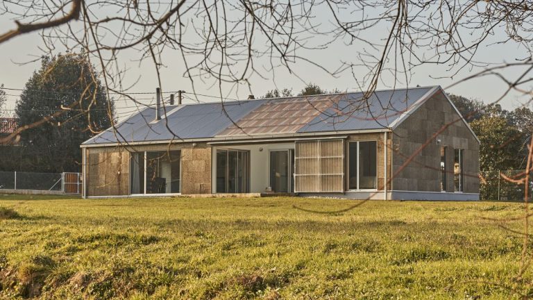 Moderný jednopodlažný dom so stenami z laminátového dreva a veľkými oknami, obklopený zeleným trávnikom.