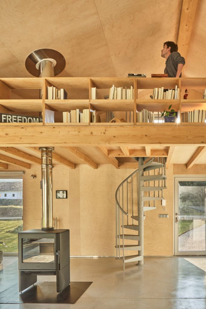 Nadčasová obývačka s krbovými kachľami, točitým schodiskom a drevenou galériou s knižnicou.