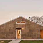 Predná strana moderného jednopodlažného domu so stenami z laminovaného dreva v minimalistickom dizajne.