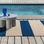 Pruhovaný koberec O deck Electric Blue s nízkym stolom pri bazéne.