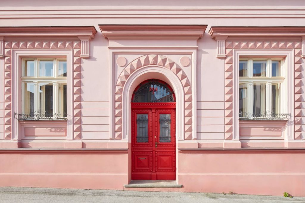 Detail historickej fasády budovy s červenými dverami a ozdobnými prvkami.