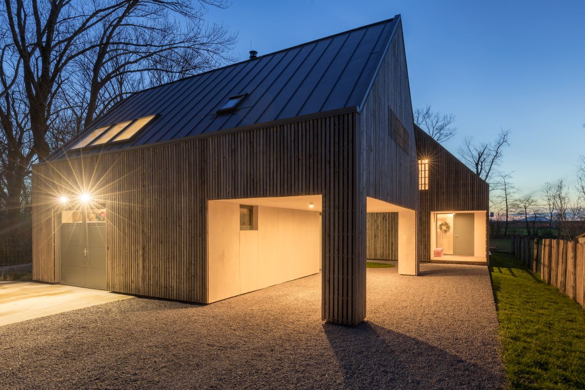 Exteriér moderného domu pri západe slnka s osvetlenými vchodmi a garážou.