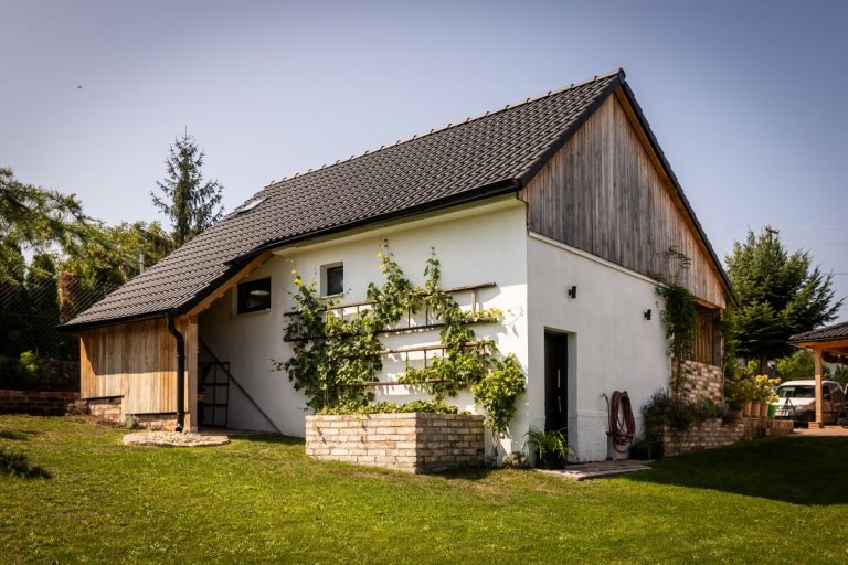 Tradičný rodinný dom s modernou strechou, obklopený zeleným trávnikom a popínavými rastlinami na fasáde.