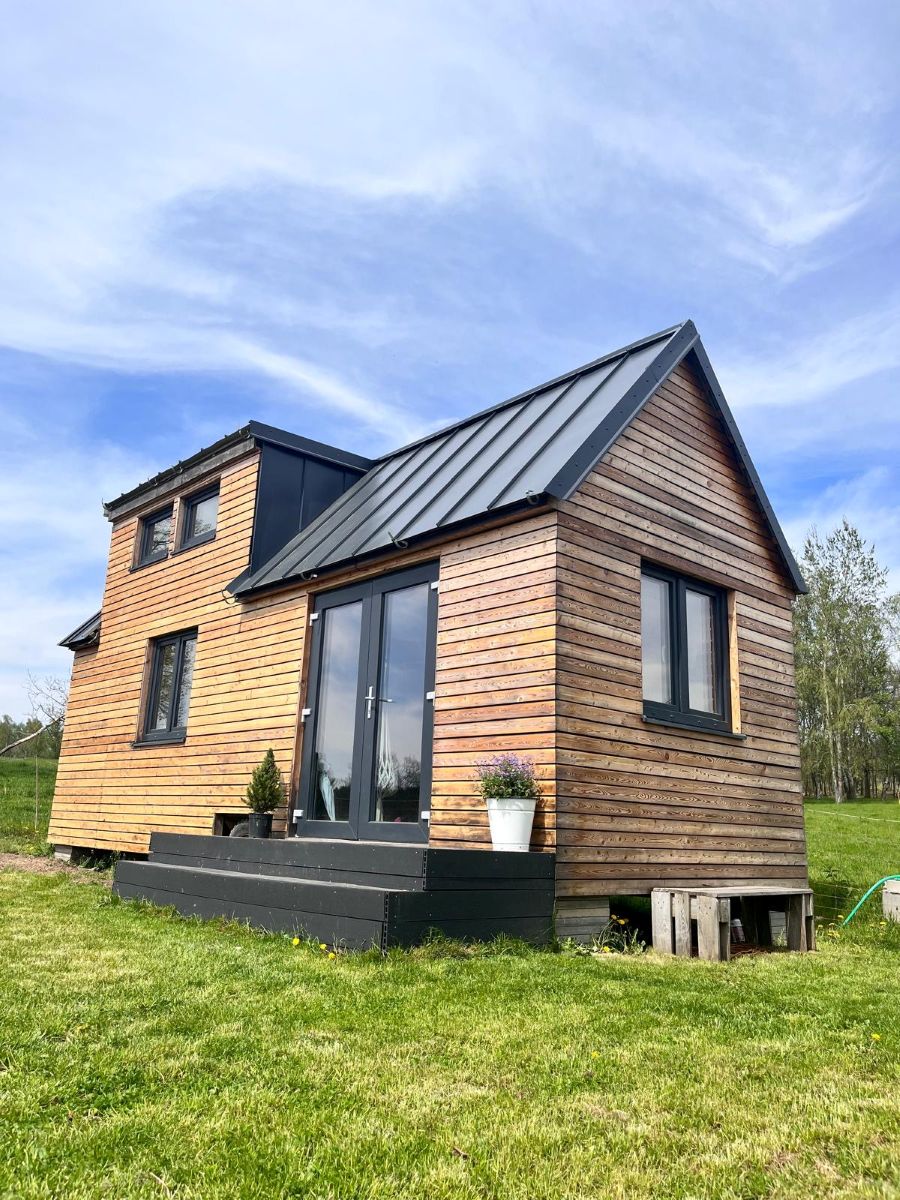 Tiny house s dreveným obkladom a čiernou strechou.