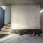 Interiér chaty VA House s betónovými stenami a drevenými schodmi.