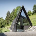 Presklená predná časť chaty VA House s výhľadom na svah a les.