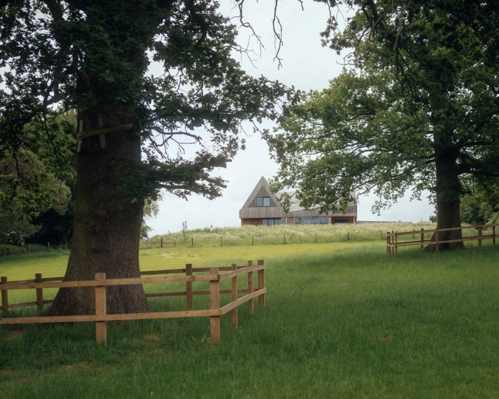 Dom Water Farm viditeľný cez stromy a drevený plot na rozkvitnutej lúke.