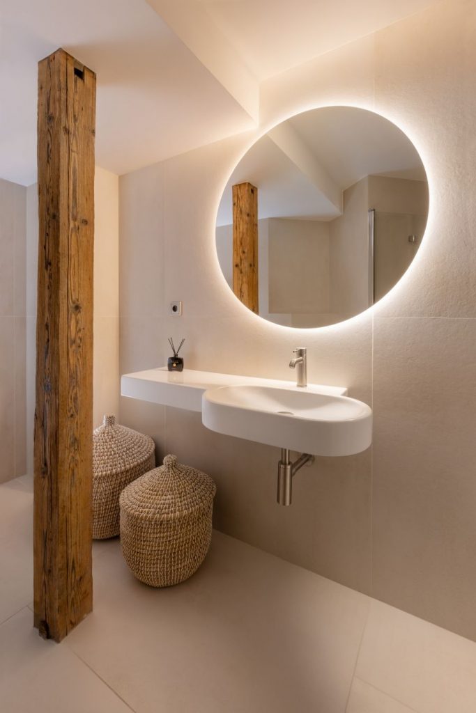 Minimalistická kúpeľňa v podkroví s podsvieteným zrkadlom, bielym umývadlom a prírodnými materiálmi.