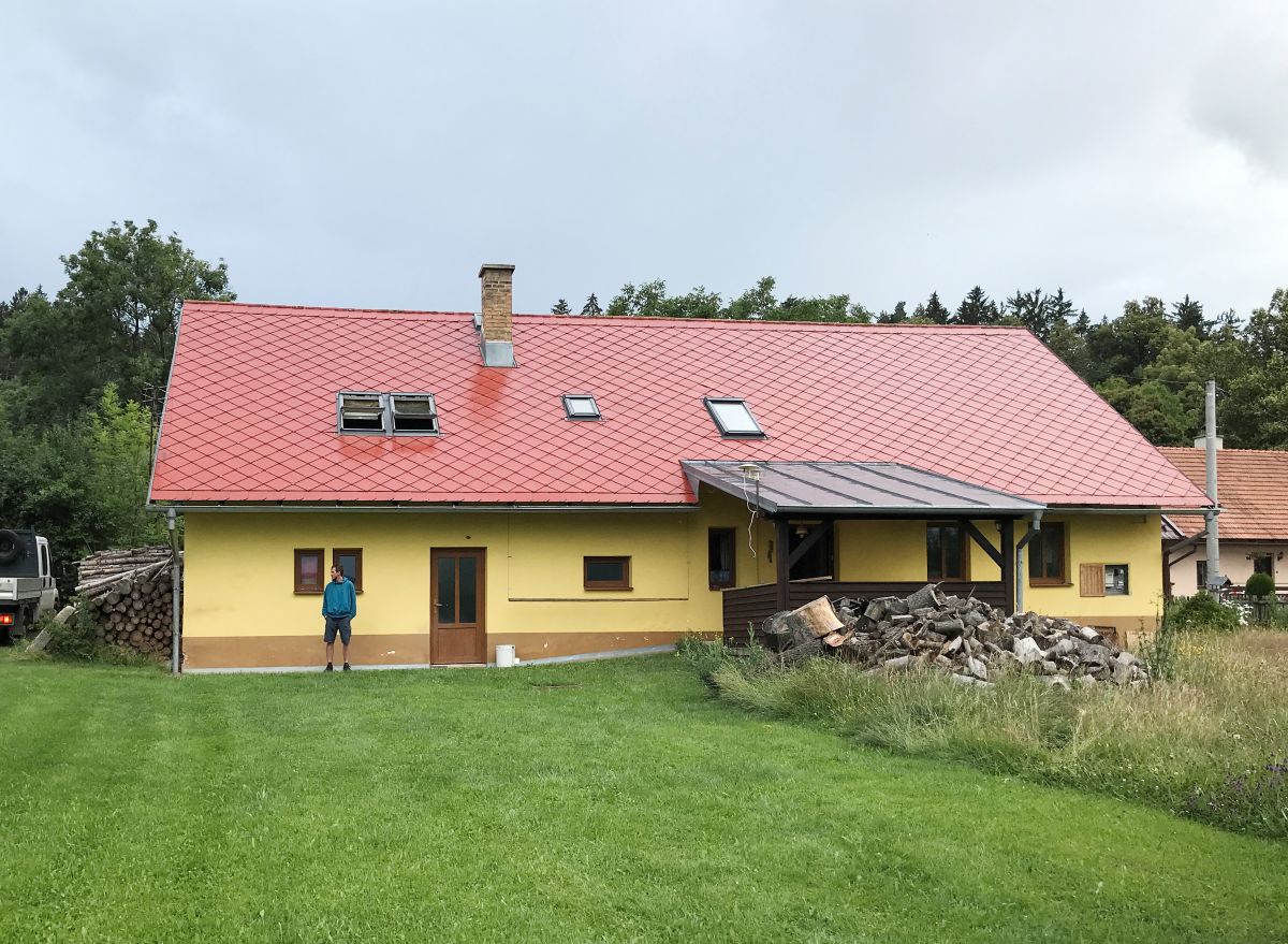 Klasická chalupa s červenou strechou a žltou fasádou obklopená prírodou.