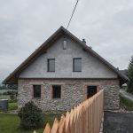 Zadná strana chalupy s kamenným základom a dreveným plotom.