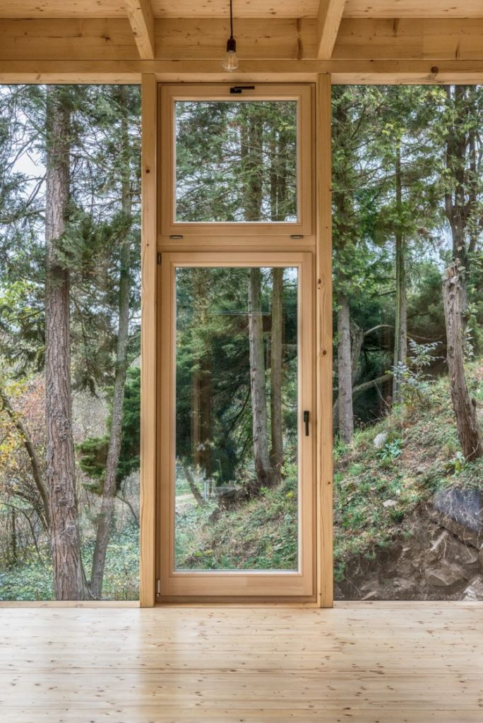 Sklenené dvere v drevenej chate vedúce na verandu s výhľadom na zeleň.