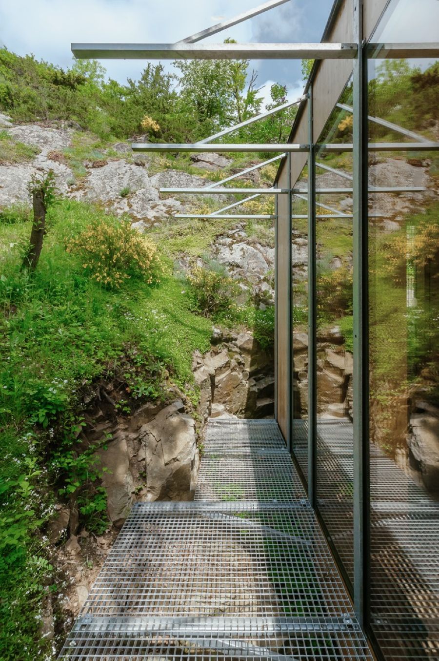 Moderný drevený domček s kovovým roštom a záhradou na pozadí.