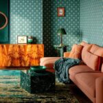 Elegantný interiér so vzorovanou tmavozelenou tapetou, smaragdový stôl, smaragdové doplnky, retro drevená skrinka, terakotová sedačka.