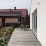 Drevená nekrytá terasa s ležadlami vedľa záhrady pri modernom dome.