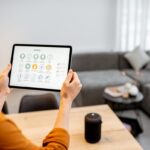 Žena drží tablet s funkciami na ovládanie smart domácnosti.